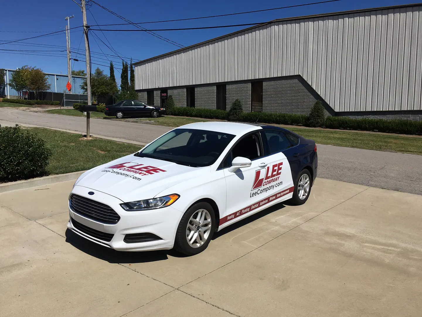 White sedan with red and black business graphics parked outside the shop