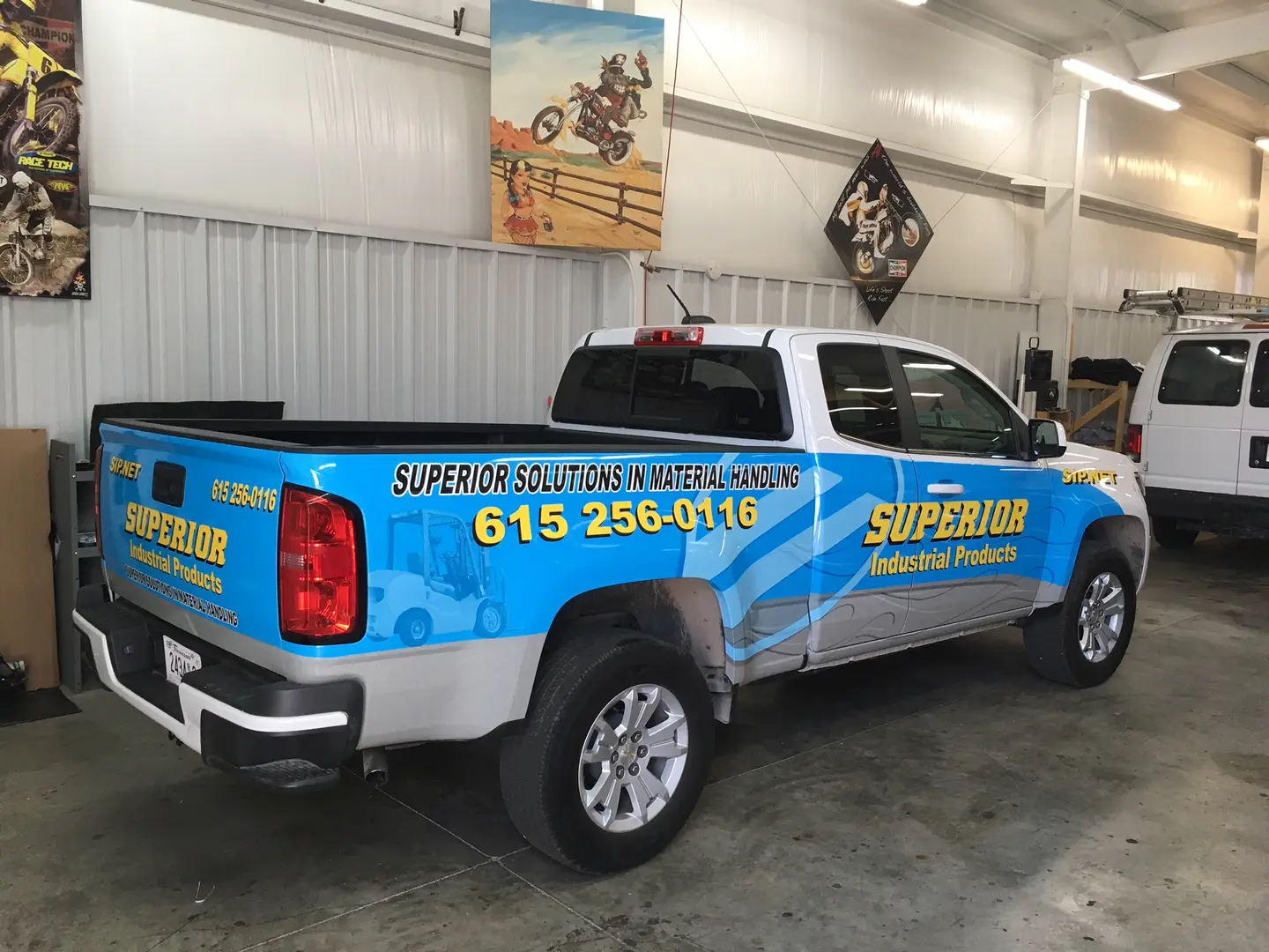 White pickup with bright blue side graphics inside the shop