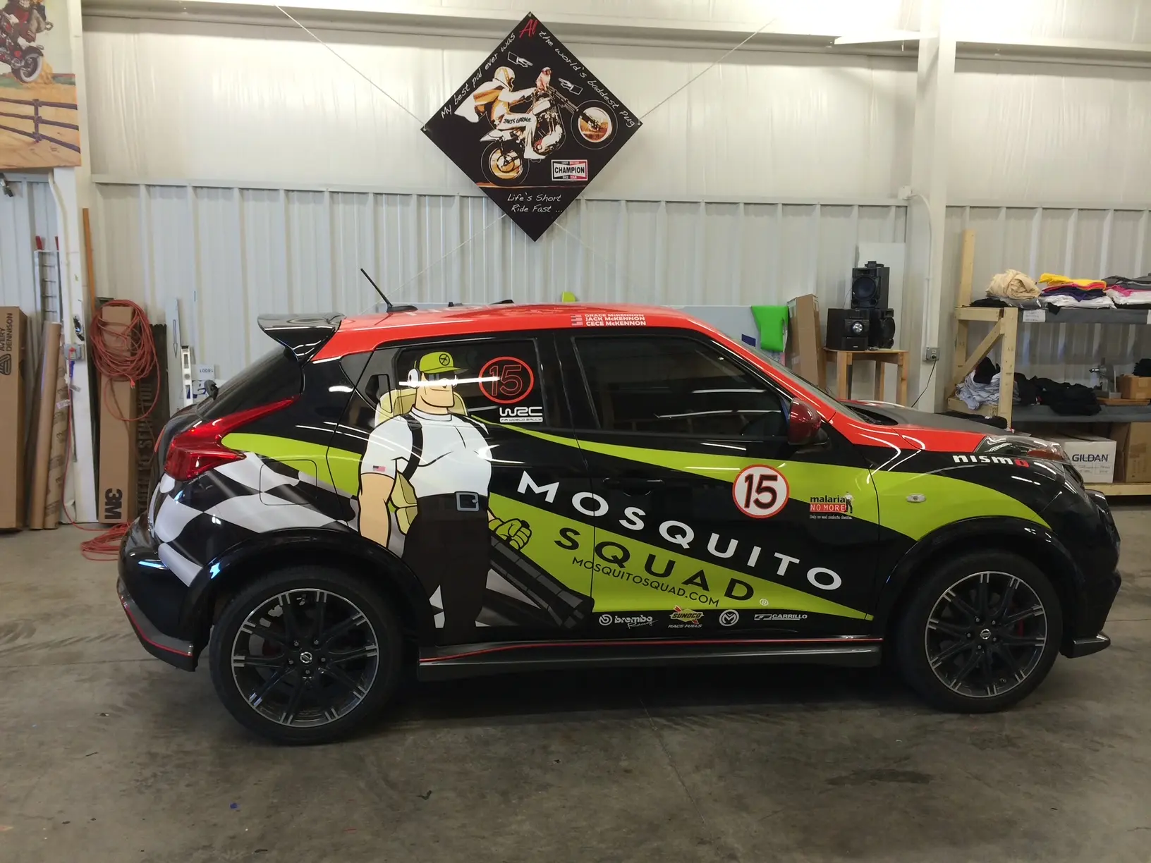 Compact car with black, red and yellow-green racing graphics inside the shop