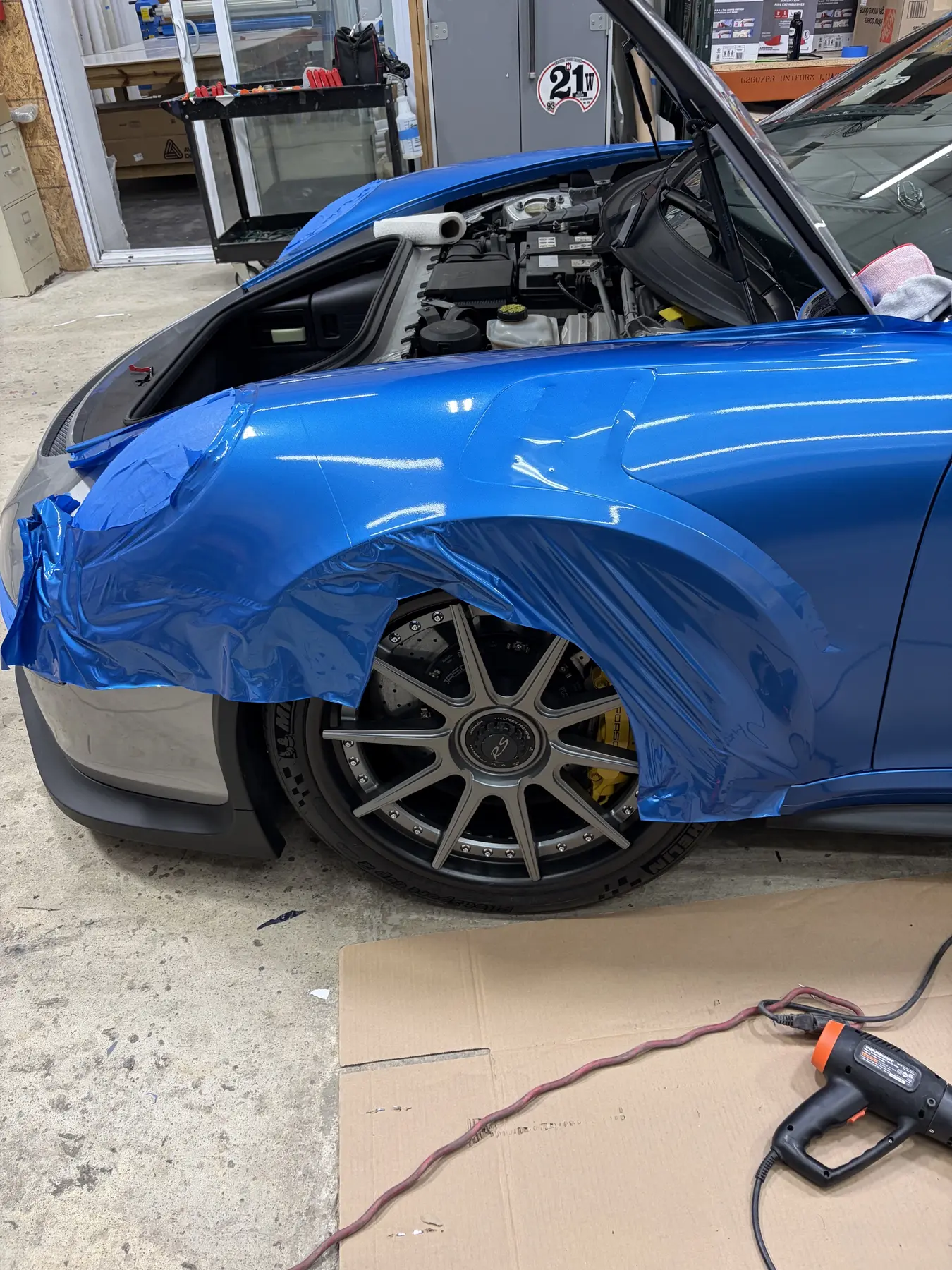 Blue wrap being applied around the front wheel and fender of a car