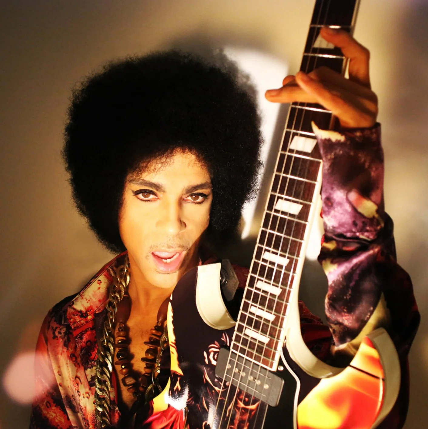 Close-up photograph of Prince holding the graphic-wrapped guitar upright beside his face