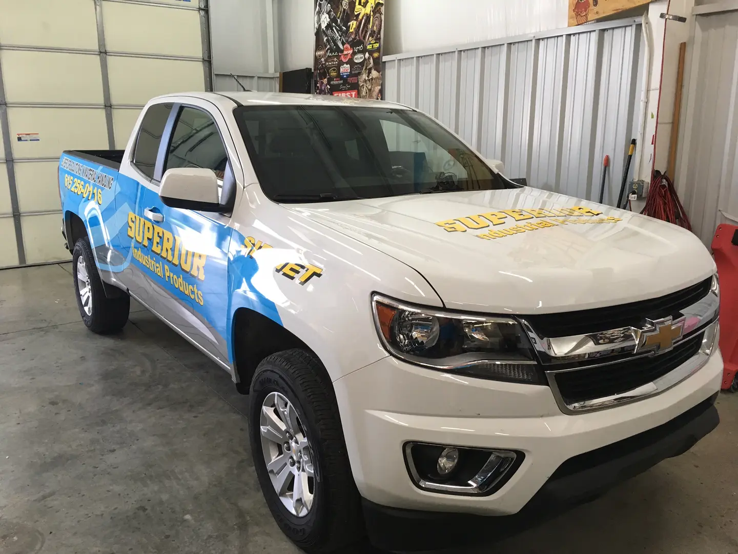 White pickup with blue and yellow side graphics inside the shop